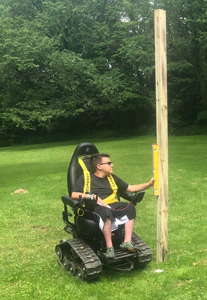 A TracFab rider checking a wooden post with a spirit level on a grassy property.