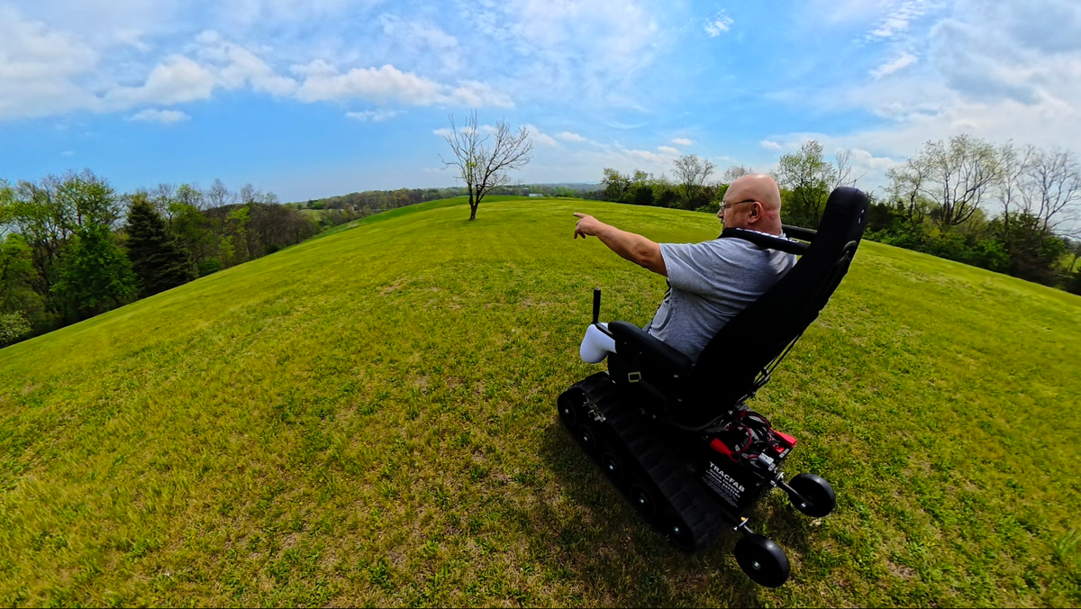 TracFab owner riding across a green field and pointing toward the open landscape.